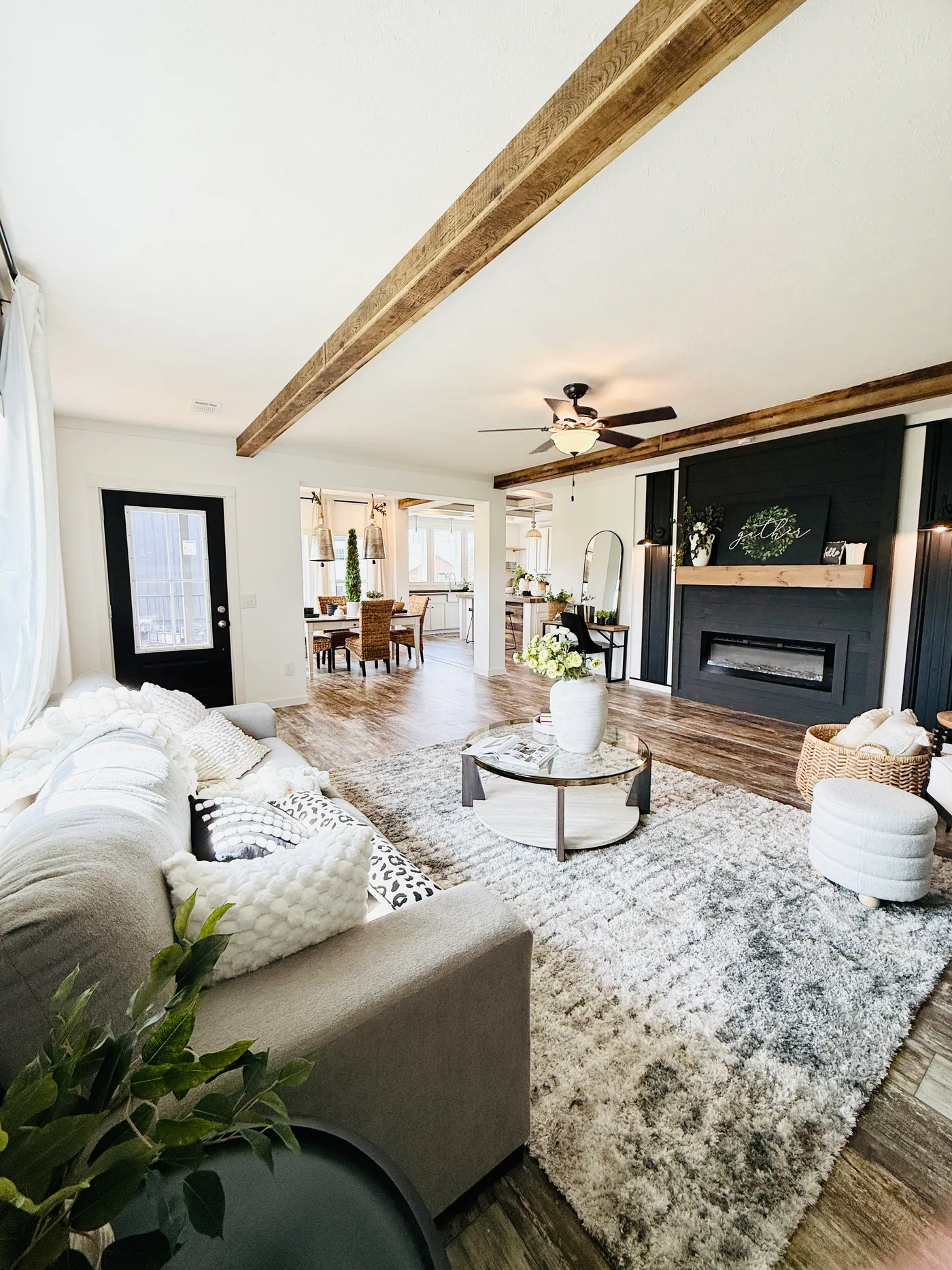 This spacious living room showcases stunning rustic beams, beautiful flooring, and a striking fireplace feature wall that creates the perfect focal point. The open layout provides plenty of room for relaxing or entertaining, while the modern farmhouse design adds warmth and character throughout. Large, inviting spaces like this make it easy to gather with family and friends while enjoying the comfort and style of the home.