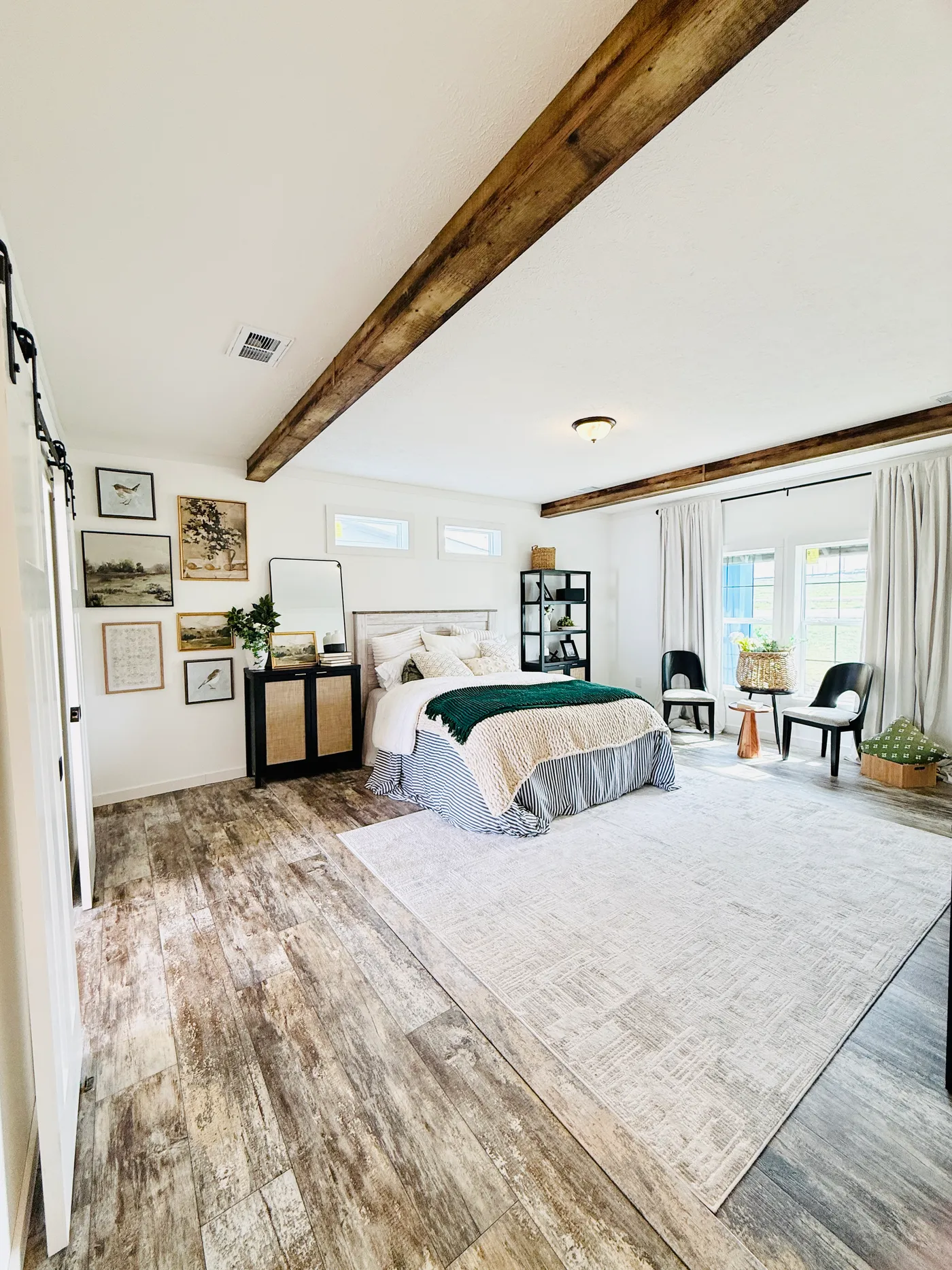 This spacious primary suite offers the perfect combination of comfort and style, featuring beautiful wood beam accents, modern flooring, and plenty of room for a full bedroom setup. The sliding barn doors add character while providing easy access to the private ensuite bathroom. With its open layout and warm farmhouse touches, this bedroom creates a relaxing retreat at the end of the day.