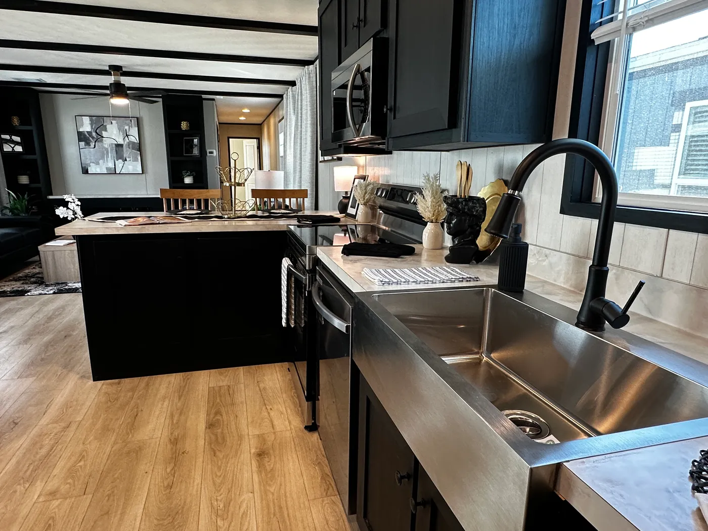 Beautiful 3 bedroom, 2 bathroom manufactured home featuring a modern charcoal interior and open-concept design. The stylish kitchen includes stainless steel appliances, a stainless steel farmhouse sink, and ample cabinet space. The spacious living room offers a built-in entertainment center with electric fireplace, perfect for relaxing or entertaining. The private primary suite features a tiled low-profile walk-in shower, a large garden soaking tub, and generous storage. This home combines affor