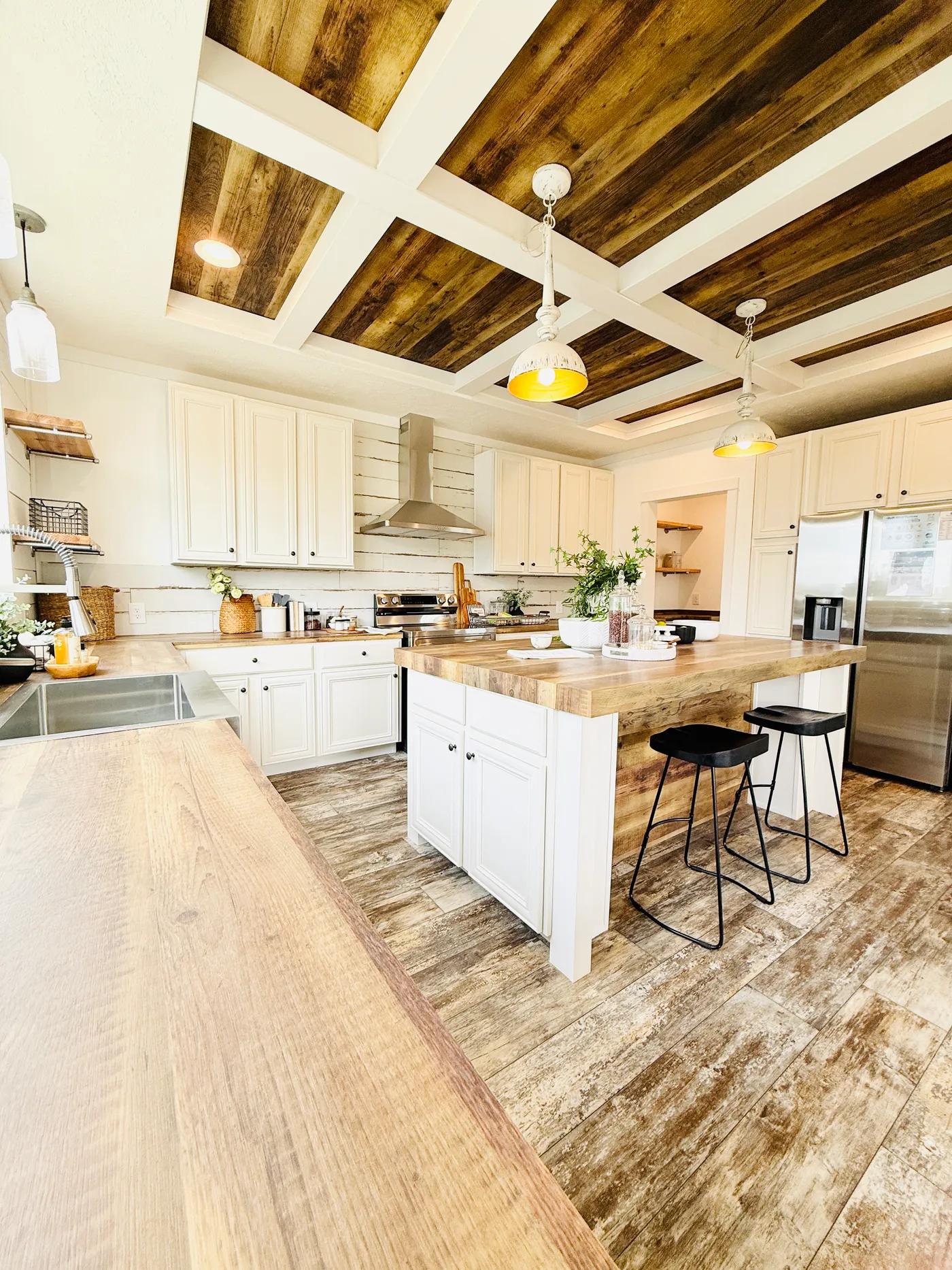 This stunning kitchen is the heart of the home, featuring a large center island with seating, beautiful countertops, and plenty of workspace for cooking and entertaining. The custom coffered ceiling with wood accents adds warmth and character, while the white cabinetry and stainless steel appliances create a bright, modern farmhouse feel. With abundant storage, stylish lighting, and an open layout that flows into the living areas, this kitchen is both functional and impressive.