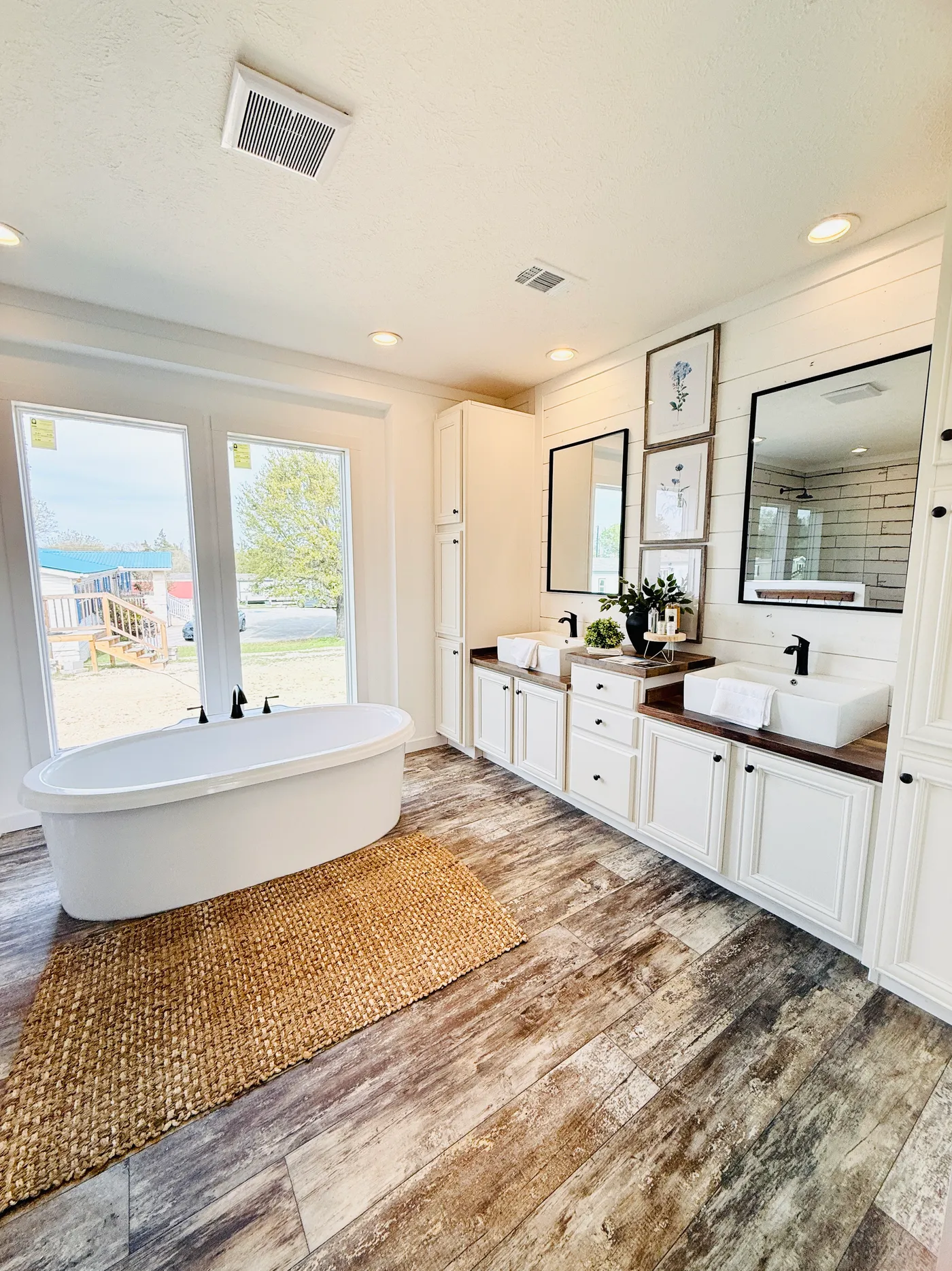 This luxurious primary bathroom offers a spa-like retreat with a beautiful freestanding soaking tub perfectly positioned beneath large windows for natural light. The spacious walk-in shower features stylish tile work and modern fixtures, while the extended vanity provides plenty of storage and counter space. Designed with both comfort and elegance in mind, this bathroom creates the perfect place to relax and unwind.